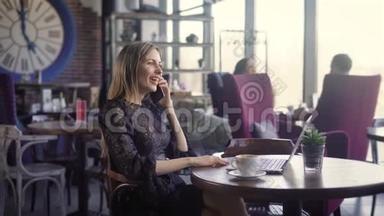 快乐的年轻女人在咖啡店里打电话和使用电脑。 一个美丽的女孩，<strong>情感交流</strong>